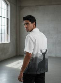 Man wearing a white shirt with a deer silhouette design in a minimalistic room.