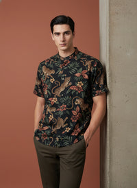 Man wearing a patterned shirt leaning against a wall.