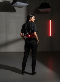 Person wearing a black outfit with a red accent in a dark room with red light.