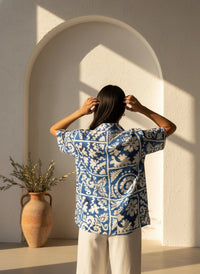 Person wearing a blue and white patterned shirt standing in front of a sunlit archway.