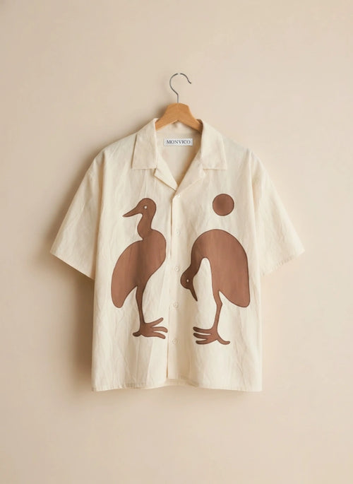 Beige shirt with brown duck designs on a hanger against a beige background