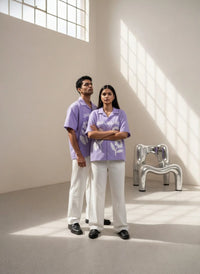 Two people wearing matching purple and white outfits standing in a bright room with large windows.