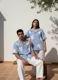 Two people sitting on a bench wearing matching blue checkered shirts with white floral patterns.