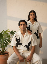 Two people wearing matching white shirts with black bird patterns in a minimalistic setting.