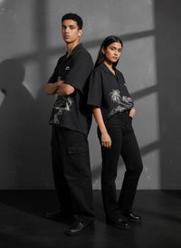 Two people wearing black outfits with palm tree designs against a gray background