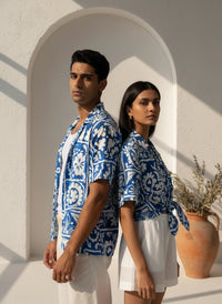 Two people wearing blue patterned shirts standing in front of a white archway.