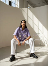 Person wearing a purple floral shirt sitting in a sunlit room.