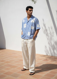 Man wearing a blue checkered shirt with floral patterns and white pants standing on a tiled floor.