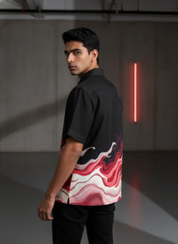 Man wearing a black shirt with a colorful abstract design in a modern indoor setting.