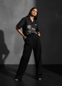 Woman wearing a black outfit with a palm tree design against a dark background