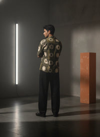 Person wearing a patterned jacket standing in a dimly lit room with a light fixture and a red cube.
