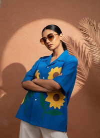 Woman wearing a blue shirt with sunflower designs against a brown background