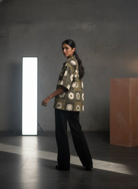 Woman wearing a patterned shirt and black pants standing in a dark room with a light source.