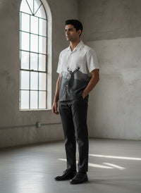 Man wearing a white shirt with a deer design and dark pants in a room with large windows.